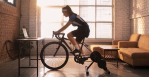 woman at home in apartment setting using stationary bike in front of laptop