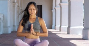 woman seated in cross legged yoga pose hands in prayer position