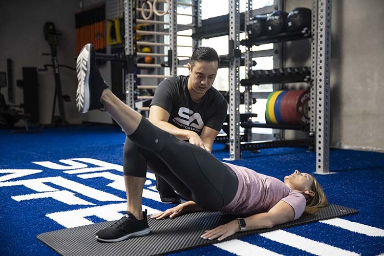 gym professional mobility trainer informing three client in hip extension exercise