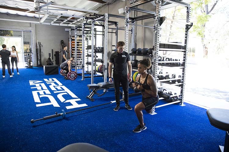 gym with three professional trainers informing three clients in various exercises